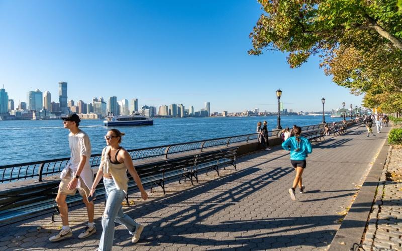 people walking on a sidewalk near a body of water and a city
